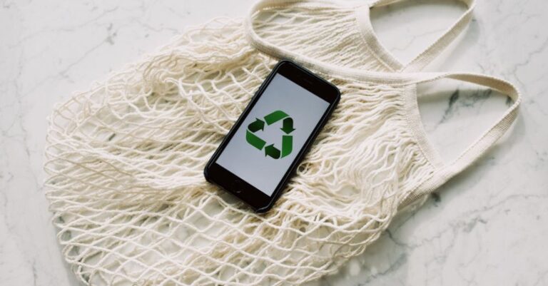 Conserve - Overhead of smartphone with simple recycling sign on screen placed on white eco friendly mesh bag on marble table in room